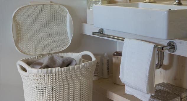 Nyitott fedelű, fonott mintás szennyestartó kosár a fürdőszobában, mellette mosdó és törölközőtartó. Praktikus és esztétikus tárolás a mindennapi használathoz.
