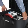 Kép 8/9 - Fekete, kerekes szerszámosláda, félig nyitva, benne különböző szerszámok láthatók, például fehér elektromos eszköz és piros kábelek. A láda oldalán fogantyúk segítik a szállítást, kézben tartva használva.
