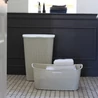 Kép 2/3 - Krémszínű CURVER 'MY STYLE' rattan szennyestartó 55L, modern fürdőszobai környezetben, ívelt fedéllel a maximális helykihasználásért. Mellette egy kis tároló kosár friss törölközőkkel.