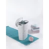 Kép 5/7 - Modern, fehér CURVER 'RIBBON' szennyestartó 49 L, nyitott fedéllel, elegáns szalaghatású formával. Mellékeleg tetszetős türkiz szőnyegen egy halom puha, színes törölköző látható, melyek rendben várják a használatot.