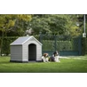 Kép 5/8 - Modern, szürke KETER kutyaház fűben, mellette két kutya pihen. A kutyaház időjárásálló, megemelt padlóval rendelkezik, és tágas belső teret kínál a kényelemhez. Zöld kerítés és fák láthatók a háttérben.