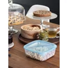 Kép 7/8 - Transzparens, kék fedéllel ellátott CURVER 'Fresh&amp;Go' szögletes ételtartó, 2,9 liter űrtartalommal, földimogyoróval töltve. A faasztalon, édes sütemények és italok mellett látható, természetes otthoni környezetben.