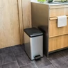 Kép 7/7 - Modern, ezüst színű CURVER 'SLIM BIN' pedálos szemetes, 25L űrtartalommal, keskeny kialakítással, kényelmes pedállal. Konyhában, fényes felületen, szürke csempe háttér előtt helyezkedik el, ideális a szelektív hulladékgyűjtéshez.