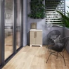 Kép 3/4 - Modern, bézs/sárga színű KETER Split Premium Wood szelektív hulladékgyűjtő a teraszon, zárható rekeszekkel és esztétikus fa hatású megjelenéssel. A háttérben zöld növényfal és kényelmes fekete szék található.