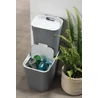 Kép 10/10 - Sötét szürke CURVER 'Ready to Collect' szelektív hulladékgyűjtő, 10L űrtartalommal, fehér tetővel és praktikus fogantyúval. Használat közben üvegeket tárol, modern konyhában elhelyezve, mellette zöld növény.