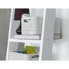 Kép 5/5 - Fekete lámpával és könyvekkel ellátott fehér polcon elhelyezett CURVER 'STYLE' S méretű rattan kosarak, krémszínben, különböző tárolt tárgyakkal. A kosarak kényelmes fogantyúval rendelkeznek, és egymásra tehetők.