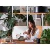 Kép 3/4 - Fiatal nő dolgozik otthoni környezetben, zöld növények és CURVER "Jute" tároló kosarak veszik körül; a természetes elemek nyugodt, inspiráló hangulatot teremtenek a munkaasztal körül.